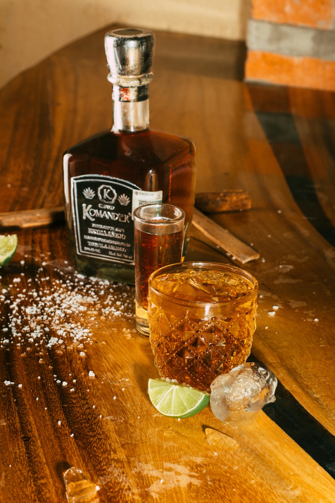 A tequila pour set on a wooden table, warm light, lime and salt, no faces.